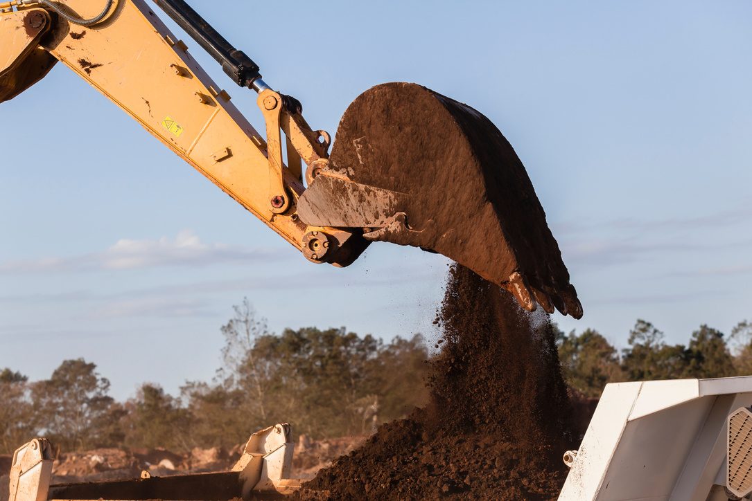 Excavator bucket unloading soil at a project site